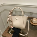 Minimalist beige lychee grain bucket bag with silk scarf and gold hardware on a table - With Pendant / Khaki