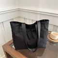 Large black nylon tote bag with wide straps and side pockets on a wooden glass table - Black