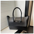Detail of minimalist black tote bag with litchi texture and long handles in home office setting - Black