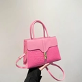 Sac à main rose en simili cuir avec texture crocodile et boucle dorée tenu à la main - Rose