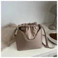 Detalle del bolso de cubo con cordón y funda de cuero en forma de U sobre una mesa blanca - Caqui