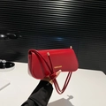 Red matte leather underarm bag with gold logo and knotted strap on dark background - Red