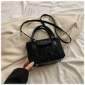Black quilted bucket bag with top handle and crossbody strap on minimalist white bedding - Black