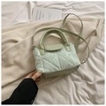 Detail view of mint green quilted crossbody bag with metal feet on textured fabric - Green