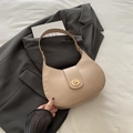 Sac hobo croissant beige chic avec fermoir doré porté sur un blazer gris foncé - Kaki
