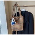 Detail of houndstooth tote bag with a cute puppy plush charm against a black blazer backdrop - With Pendant / Brown