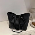 Large black faux leather tote bag with gold hardware shown in a minimalist setting - Black