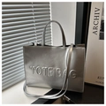 Detalle del bolso tote plateado metalizado con letras en relieve y textura de superficie ligera - Plateado