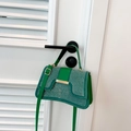 Chic green crossbody bag with silver rivet details and gold metal trim hanging on a white door - Green