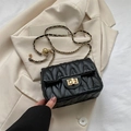 Black quilted crossbody bag with golden chain strap and square metal lock on a blazer - Black