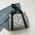 Modische silberne Stepp-Tote-Bag mit schwarzen Trägern und Seitentaschen auf Jeansjacke - Silber