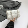 White quilted square shoulder bag with silver chain strap shown in a fashion styling context - White