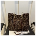 Détail du sac cabas léopard avec poignée en cuir marron et chaîne dorée sur chaise - Kaki