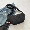 Black quilted crescent shoulder bag with knotted strap on white fabric background - Black