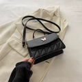 Elegante zwarte gewatteerde crossbodytas met vlindergesp op een wit colbert achtergrond - Zwart