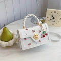 White square handbag with red cherry print and woven knot handle in a lifestyle setting - Off White