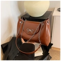 Close-up of brown glossy tote bag with silver metal bow and chain strap detail - Coffee
