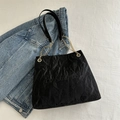 Modische schwarze Tragetasche mit Faltenstruktur und goldenem Kettenriemen auf blauem Denim - Schwarz