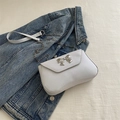 White mini crossbody bag with silver bow buckle and chain strap on blue denim background - White