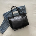 Black crocodile embossed tote bag in glossy finish on white fabric background - Black
