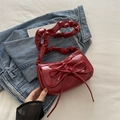 Red glossy crescent shoulder bag with bow detail and ruched strap on denim background - Red