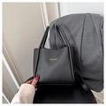 Detail van zwarte tote bag met lychee-textuur en geel logo op een grijze blazer jas - Zwart