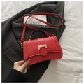 Sac à main rouge matelassé élégant avec détails dorés posé sur un blazer gris chic - Rouge