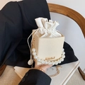Elegant cream woven bucket bag with pearl handle and golden chain strap on a wooden chair - White