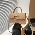 Elegante bolso bandolera beige con hebilla en D dorada y asa sobre un alféizar blanco - Caqui