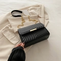 Black V-quilted faux leather crossbody bag with gold chain strap on beige blazer - Black
