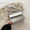 Metallic silver rectangle handbag with gold buckle on beige blazer and white bedding - Silver
