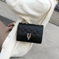 Close-up of black quilted crossbody bag featuring a gold H-shaped buckle and metal chain - Black
