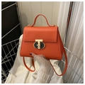 Close-up of orange leather crossbody bag featuring a unique metallic T-shaped lock - Orange