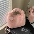 Pink faux fur handbag with leather handle and decorative tag on black background - Pink