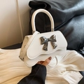 White crossbody bag featuring a large metallic bow and stylish wavy edge design - White