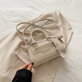 Bolso mini cuadrado blanco crema con herrajes plateados sobre un blazer beige a juego - Blanco Roto