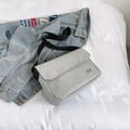 Light gray canvas messenger bag with adjustable black strap and brand label on a bed - Gray