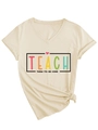 Dettaglio della maglietta beige con scollo a V, slogan 'TEACH THEM TO BE KIND' e nodo - S / Sabbia (Stampa Nera)