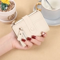 Close-up of a compact beige lychee grain leather wallet featuring zippers and a snap strap - White