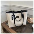 Detailed view of cream straw tote bag featuring black leather trim and gold logo detail - Black