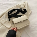 Elegante borsa a tracolla beige squadrata con ampia fascia nera su sfondo di un blazer - Bianco