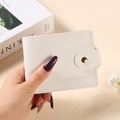 Short cream leather bifold card wallet with pebbled texture and gold snap button closure - White