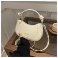 Detalle de un bolso de media luna blanco crema con asa anudada y cremallera dorada - Blanco