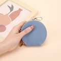 Mini porte-monnaie rond en cuir bleu clair avec fermeture éclair dorée tenue en main - Bleu