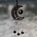 Moon-shaped suncatcher with black natural stones and moonstones hanging by the water - Shining Light