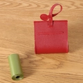 Portable red leather dog waste bag dispenser with green refill rolls on wood desk - Red