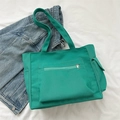 Green canvas tote bag with front zipper pocket displayed on denim jacket background - Green