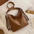 Bolso tote marrón de piel sintética con correa ajustable sobre ropa de cama blanca - Marrón