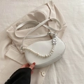 White crescent saddle bag with pearl chain and silver heart charms on beige blazer - White