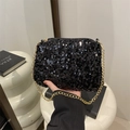 Sparkly black sequin evening bag with gold chain strap held by hand in modern setting - Black